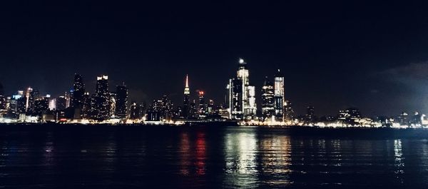 Illuminated buildings by sea against sky at night