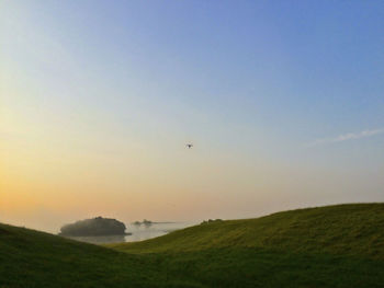 Scenic view of grassy field against sky during sunset