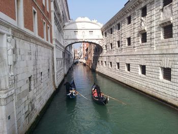 Gondolas in canal amidst buildings on sunny day in city