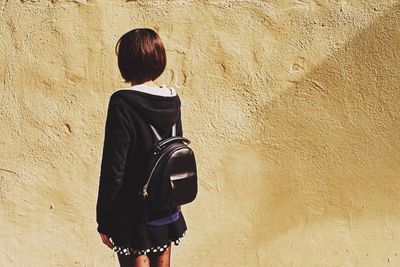 Rear view of woman with backpack standing against wall