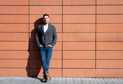 Front view of a fashionable young man standing against orange wall