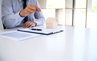 Midsection of insurance agent holding key by documents on desk