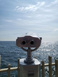 Coin-operated binoculars by sea against sky