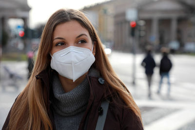 Young woman wearing mask looking away while standing outdoors