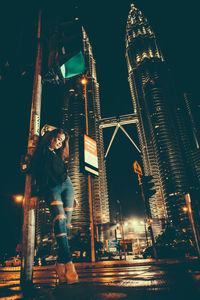 Woman standing against illuminated modern buildings in city