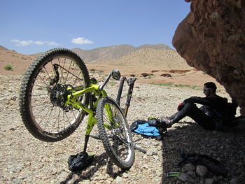 Hiker resting by punctured bicycle on sunny day