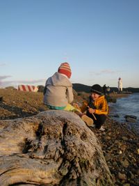 Rear view of people sitting on rock against clear sky