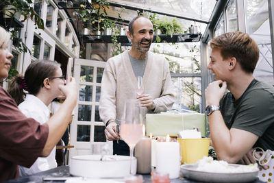 Happy man giving speech while holding drink with family at restaurant