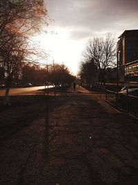 Empty road by bare trees and buildings against sky