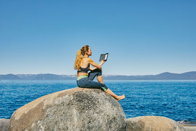 Woman sitting on rock by sea against clear sky