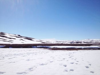 Snow covered landscape against clear blue sky