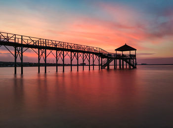 Silhouette bridge over sea against sky during sunset