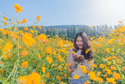 Smiling woman standing by yellow flowering plants