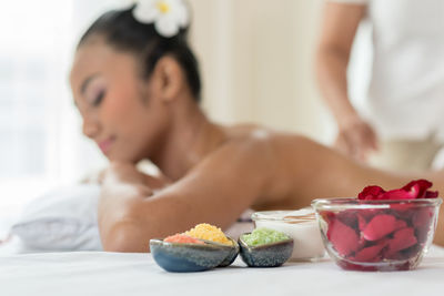 Close-up of petals with masseuse giving massage to young woman relaxing at spa