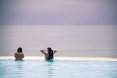 Rear view of women in infinity pool against sea