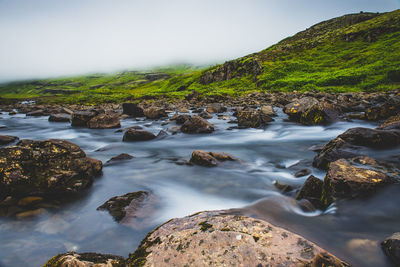 Stream flowing through rocks in sea against sky