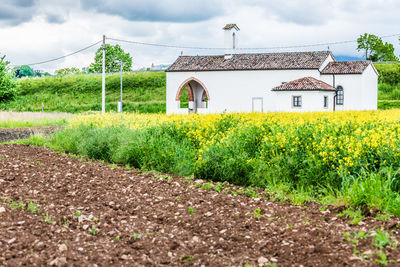 House on field by houses against sky