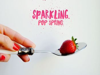 Close-up of hand holding strawberry over white background