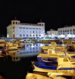 Boats moored in calm lake in front of illuminated city at night