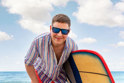 Portrait of smiling man holding surfboard while standing at beach