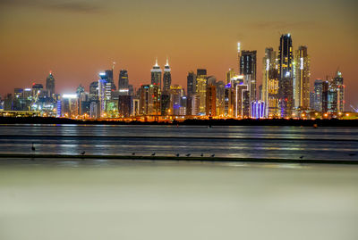 Illuminated buildings by river against sky at night