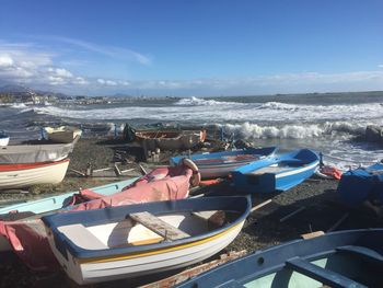 Boats moored on beach against blue sky