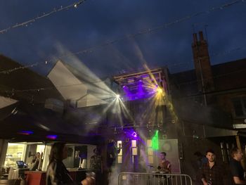 People in illuminated city against sky at night