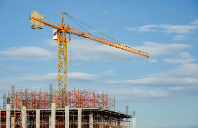 Low angle view of crane at construction site against sky