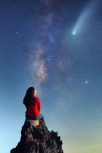 A young woman watching the beauty of the milky way and a meteor on the rocks.