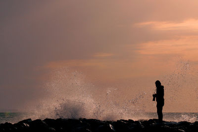 Silhouette of man in sea against sky at sunset