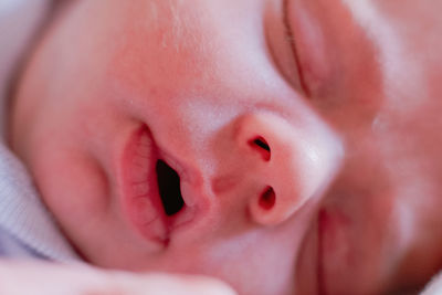 From above closeup mouth and cute nose of crop tranquil newborn with pink skin against blurred white bed sheet