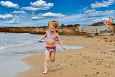 Rear view of boy running at beach against sky