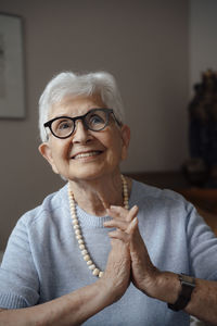 Happy senior woman with hands clasped sitting at home