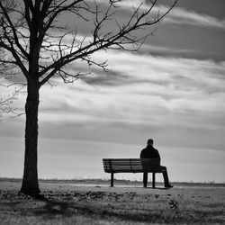 Rear view of man sitting on bench against sky