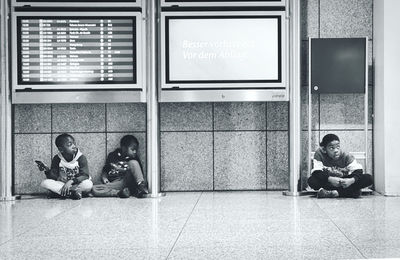 Full length of people sitting on floor against wall