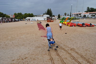 Rear view of mother pulling carriage with son at sandy beach