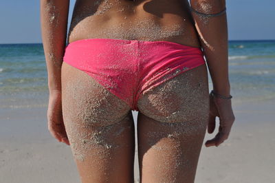 Midsection of woman in panty covered with sand at beach