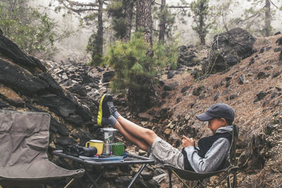Full length of boy relaxing on chair at forest