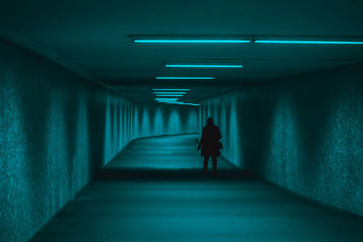 Rear view of person walking in illuminated tunnel