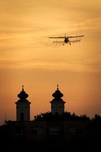 Silhouette airplane flying over church against sky during sunset