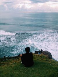 Men sitting at cliff against sea