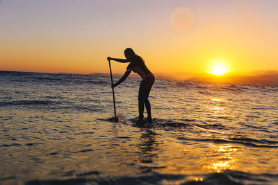 Female sup surfer at sunset time