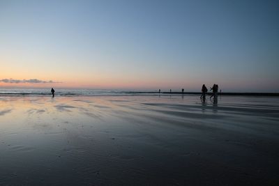 Silhouette people on beach against clear sky during sunset