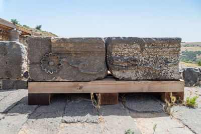 Old wooden bench on rock against clear sky
