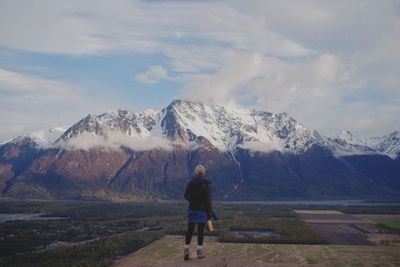 Full length rear view of woman looking at snowcapped mountains against sky