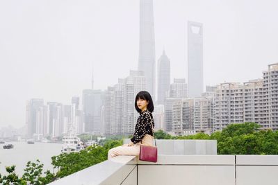 Portrait of woman sitting on buildings terrace against sky