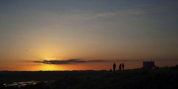 Silhouette people standing on land against sky during sunset