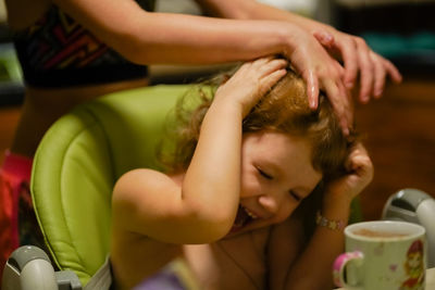 Midsection of girl massaging cheerful sister head at home