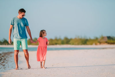 Rear view of friends standing on beach against sky