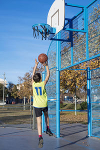 Rear view of man playing basketball hoop against blue sky